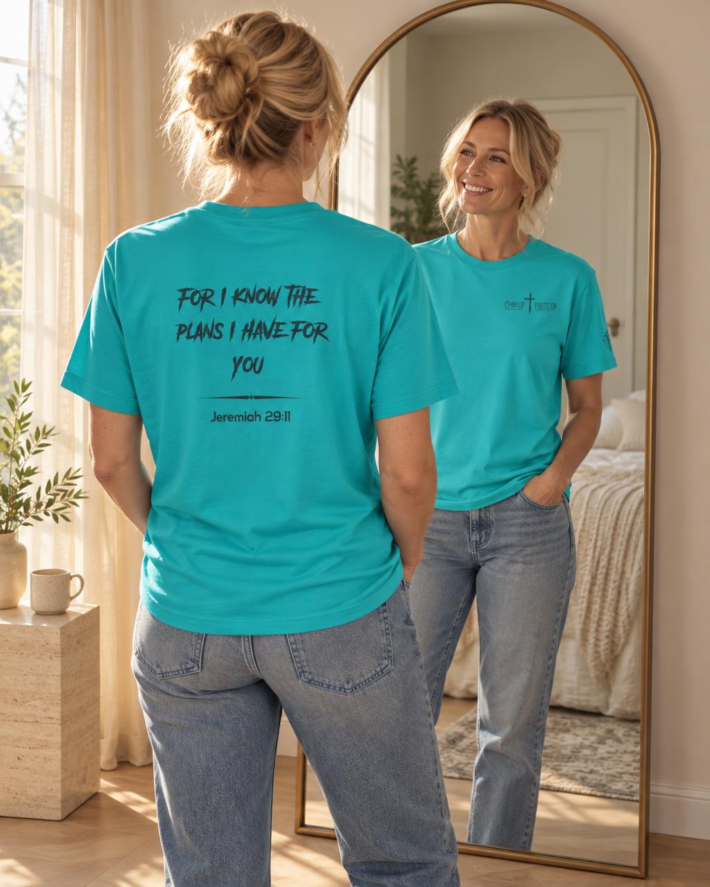 Blonde woman seen from behind in an arched mirror, wearing the teal For I Know The Plans faith tee with For I know the plans I have for you and Jeremiah 29:11 on the back, while her reflection shows the CHIN UP and PRESS ON logo on the front chest.