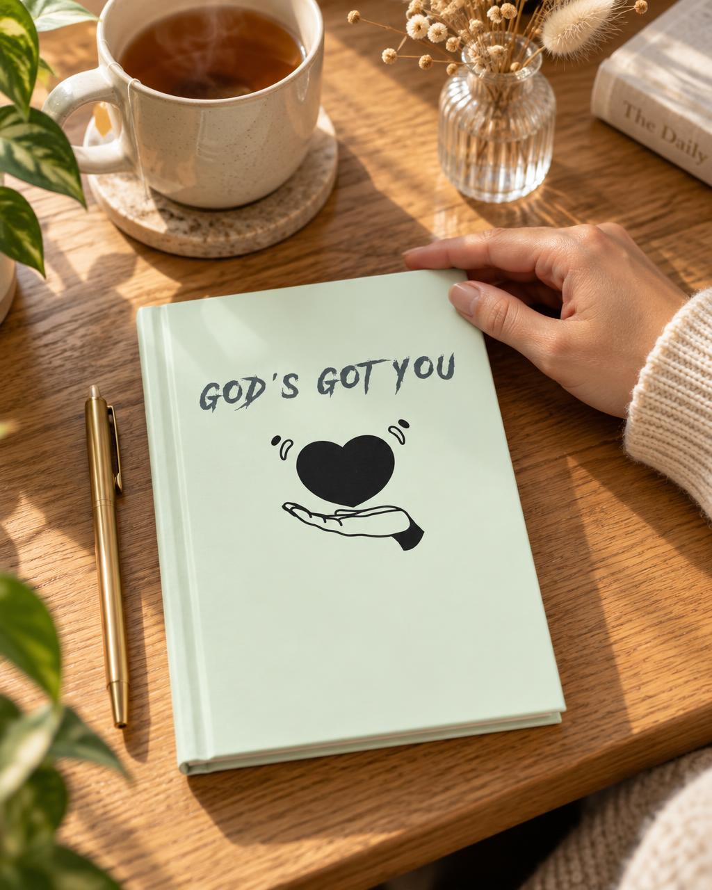 Mint green GOD'S GOT YOU journal on a wooden desk.
